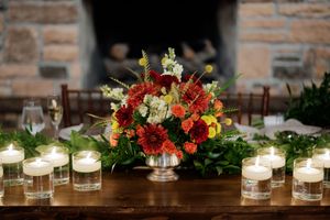 Row of lit candles and floral arrangements with autumn colors on a wooden table.