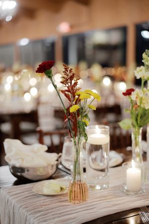 Close-up of wedding reception table decor featuring bud vases with red and yellow flowers.