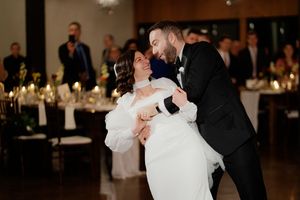 A couple shares their first dance at their wedding reception in a dimly lit ballroom with candlelit tables in the background.