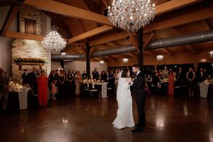 Elegant wedding reception venue with crystal chandeliers and couples dancing on a dark wood floor.