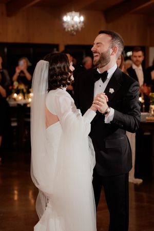 A bride in white dress and groom in black tuxedo share an intimate dance together at their wedding reception.