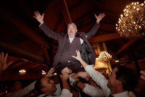 Wedding guests dancing and celebrating under elegant chandeliers at an indoor reception venue.