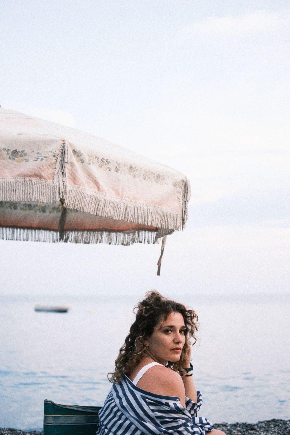 A person in a striped shirt sits by the ocean on a cloudy day at the beach.