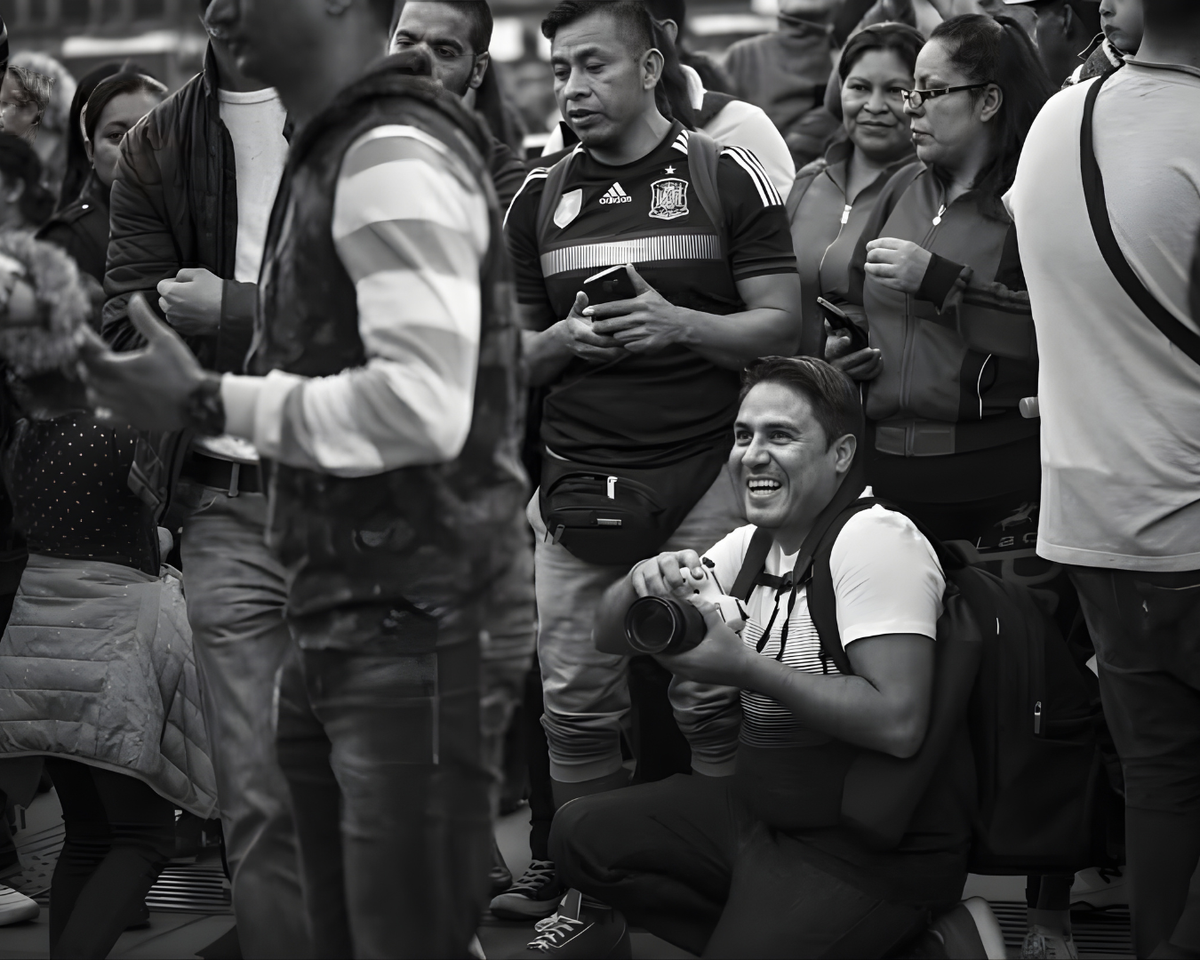 A black and white photo shows a crowd of people gathered together, some holding drinks and smiling at a social event.