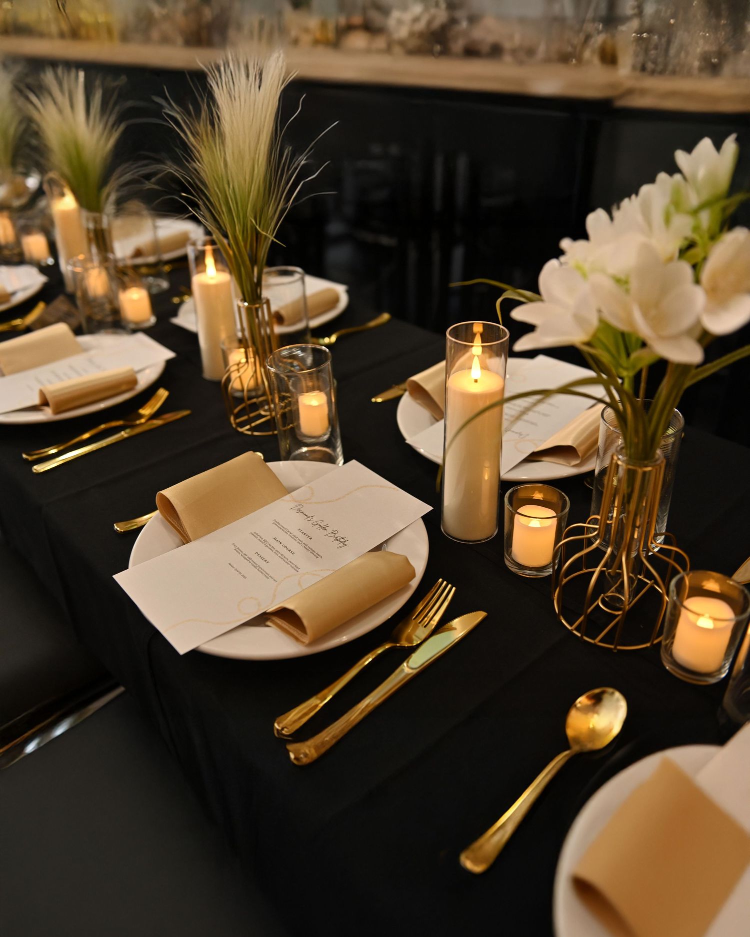 A couple poses in formal attire with a large gold ring display at an elegant indoor venue with white walls and stairs.