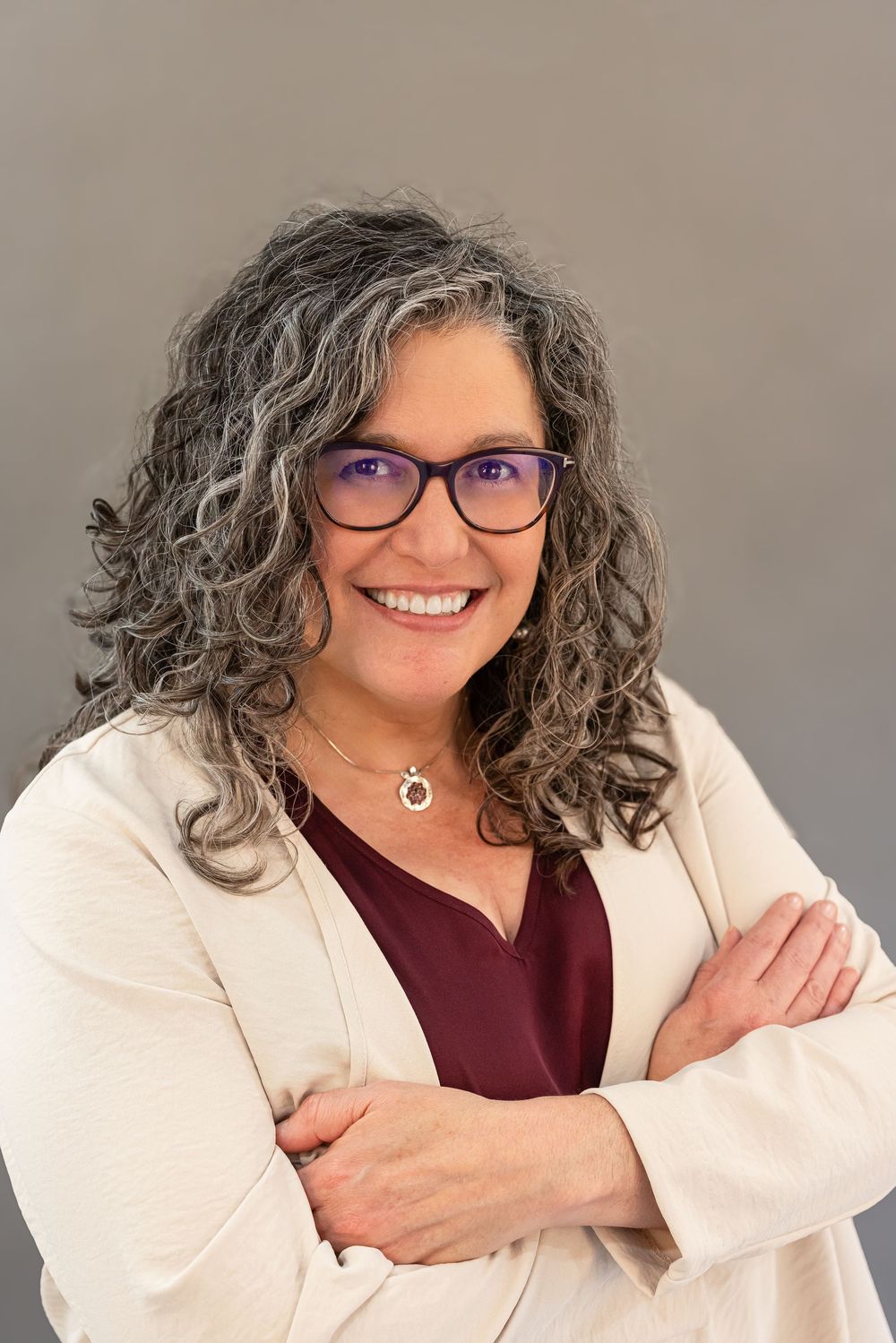 Professional headshot series showing a person in burgundy top and white blazer with curly gray hair and glasses smiling warmly.