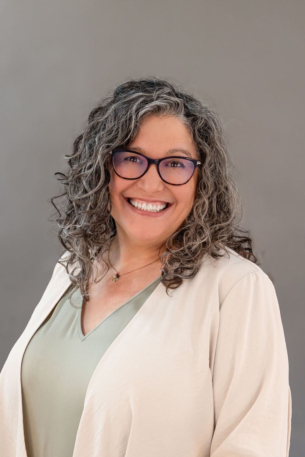 Professional headshot series showing a person with curly gray hair and glasses wearing a cream cardigan and sage top.