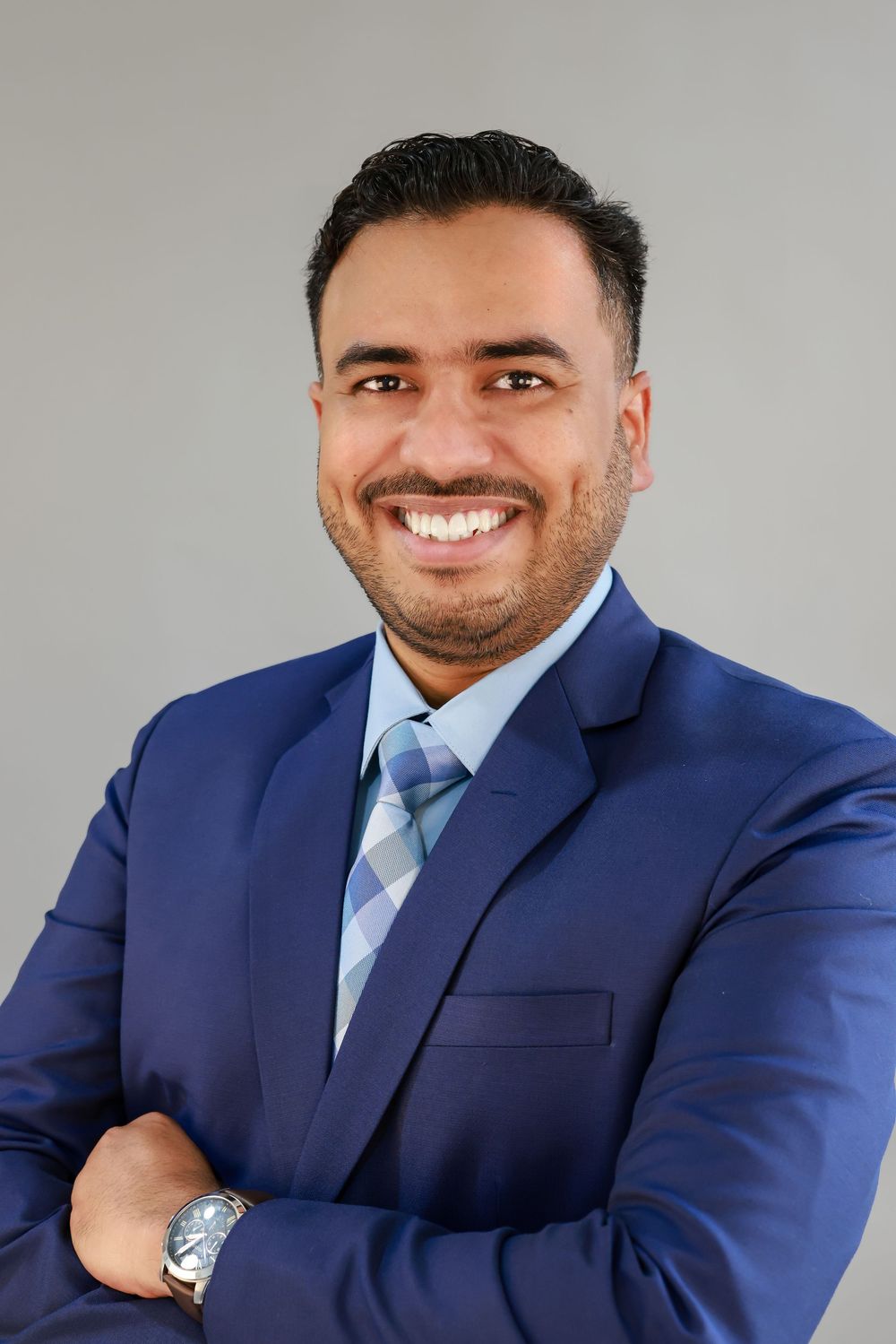 Professional headshot series showing a person in a navy blue suit and light blue tie against a gray background.