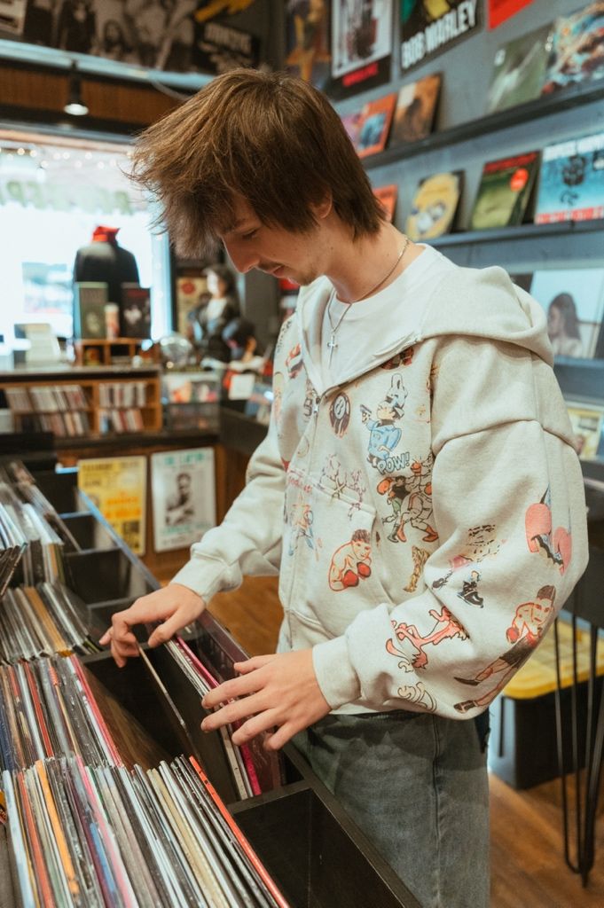 A person wearing a patterned cream hoodie browses through vinyl records at a music store.