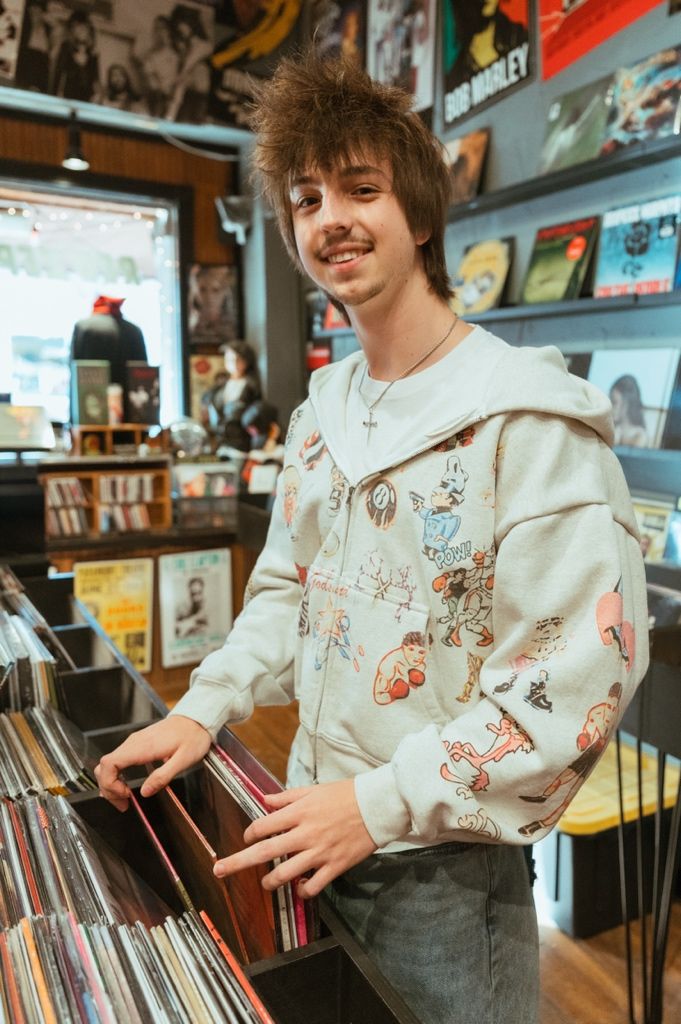 Someone browses vinyl records while wearing a cream-colored hoodie with cartoon designs in a record store.