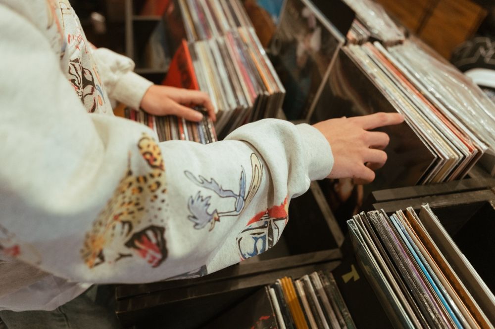 Close-up view of hands browsing through vinyl records in wooden crates at a record store.