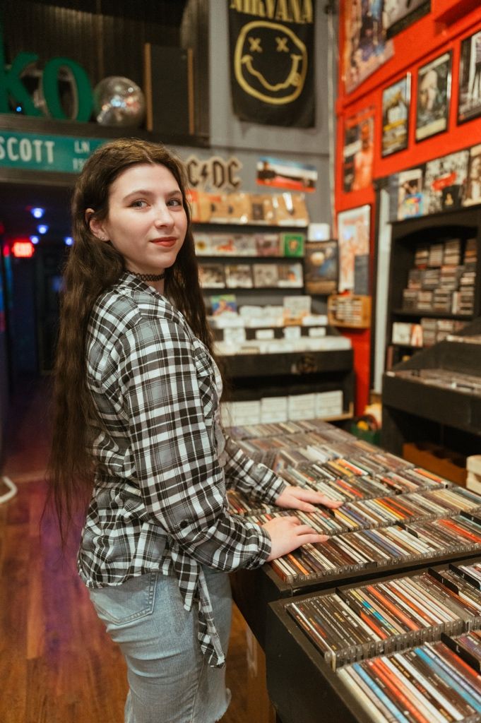 Person browsing vinyl records in a music store wearing a plaid shirt and jeans.