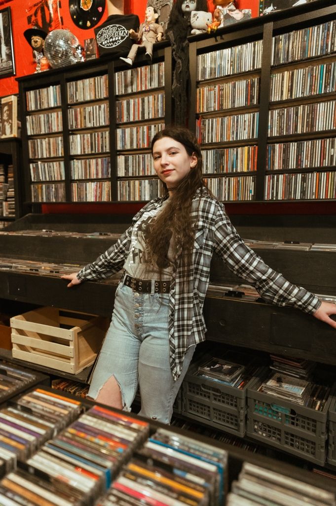 Interior of record store showing extensive wall shelving filled with vinyl albums and CDs against an orange backdrop.