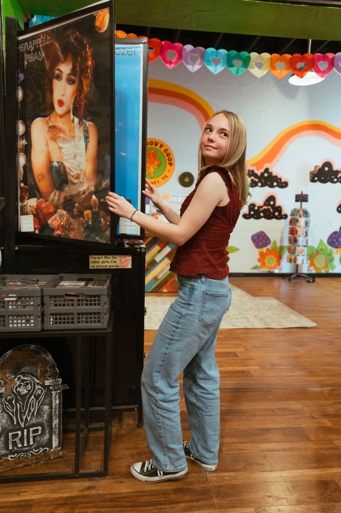 A person in jeans and red top flips through vinyl records in a colorful record store.