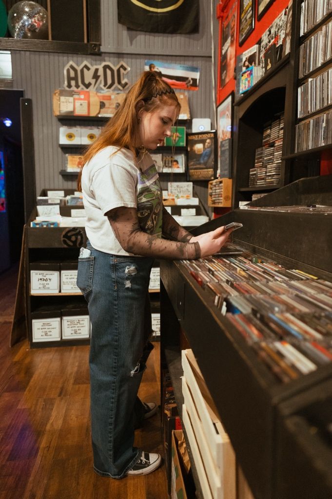 Customer browses vinyl records in a music store with AC/DC memorabilia visible on the wall.