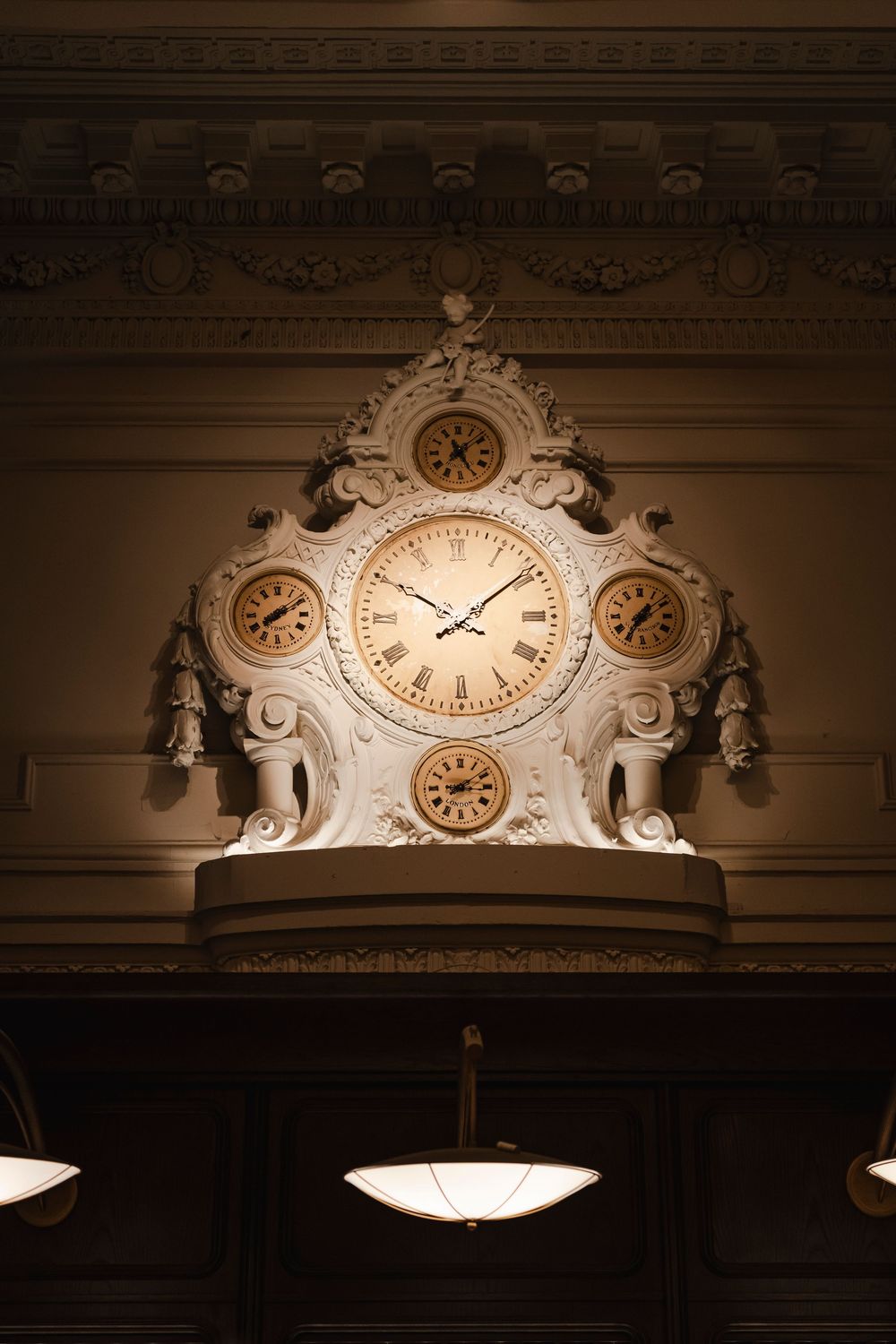 Ornate vintage clock mounted on a decorative wall molding with classical architectural details illuminated in warm light