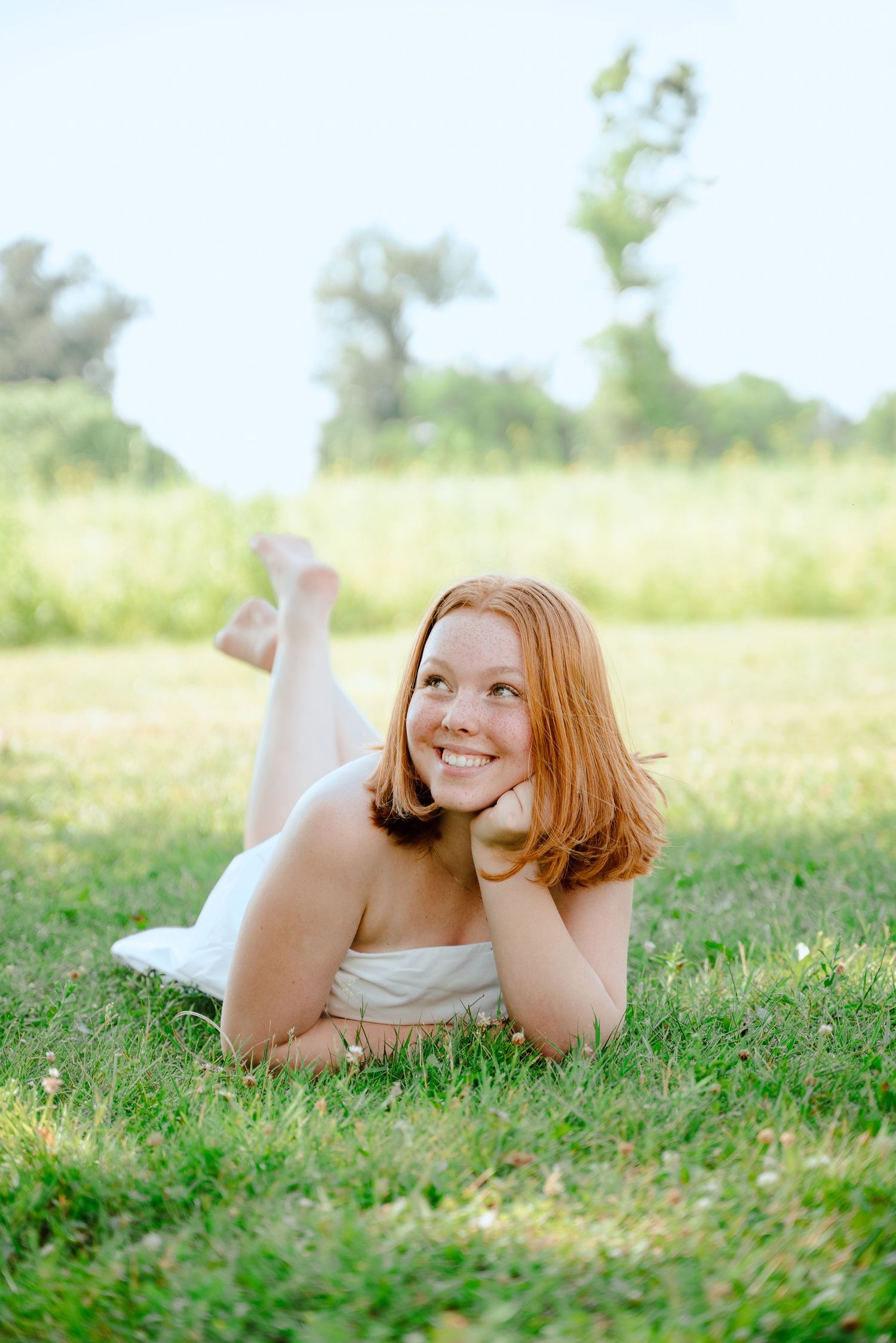A person lies on green grass in a sunny meadow wearing white clothing on a bright summer day.