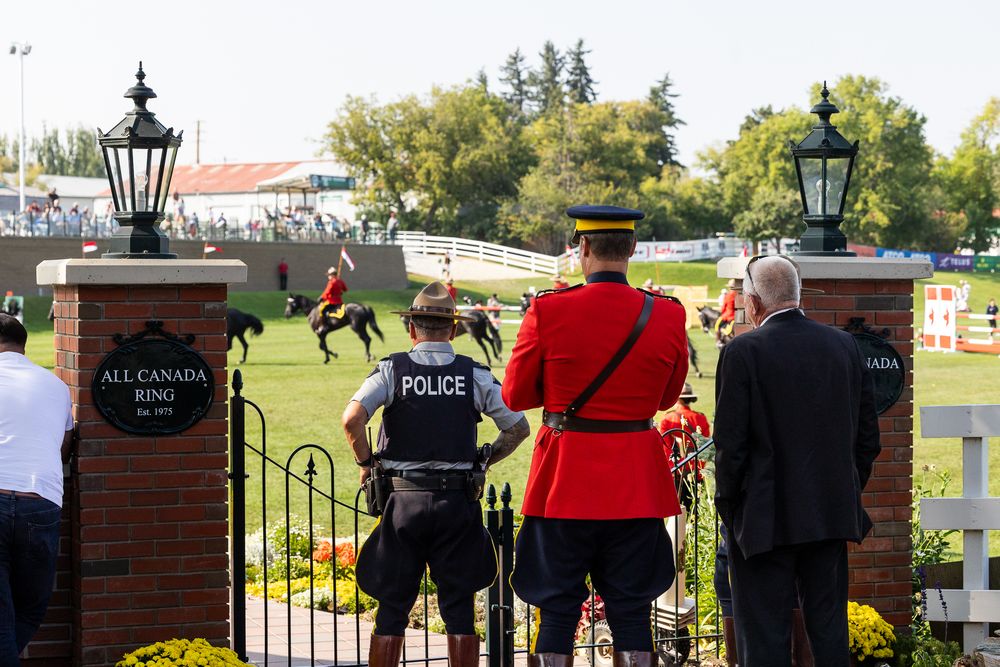 RCMP officer and police stand at the All Canada Ring gate at an equestrian event.
