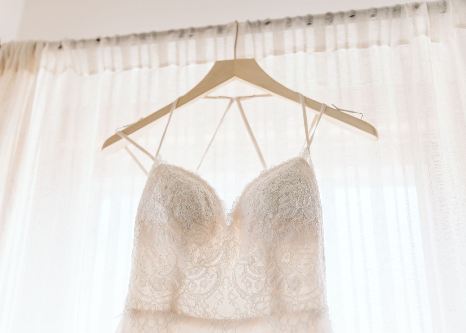 White wedding dresses hanging on hangers against sheer white curtains.