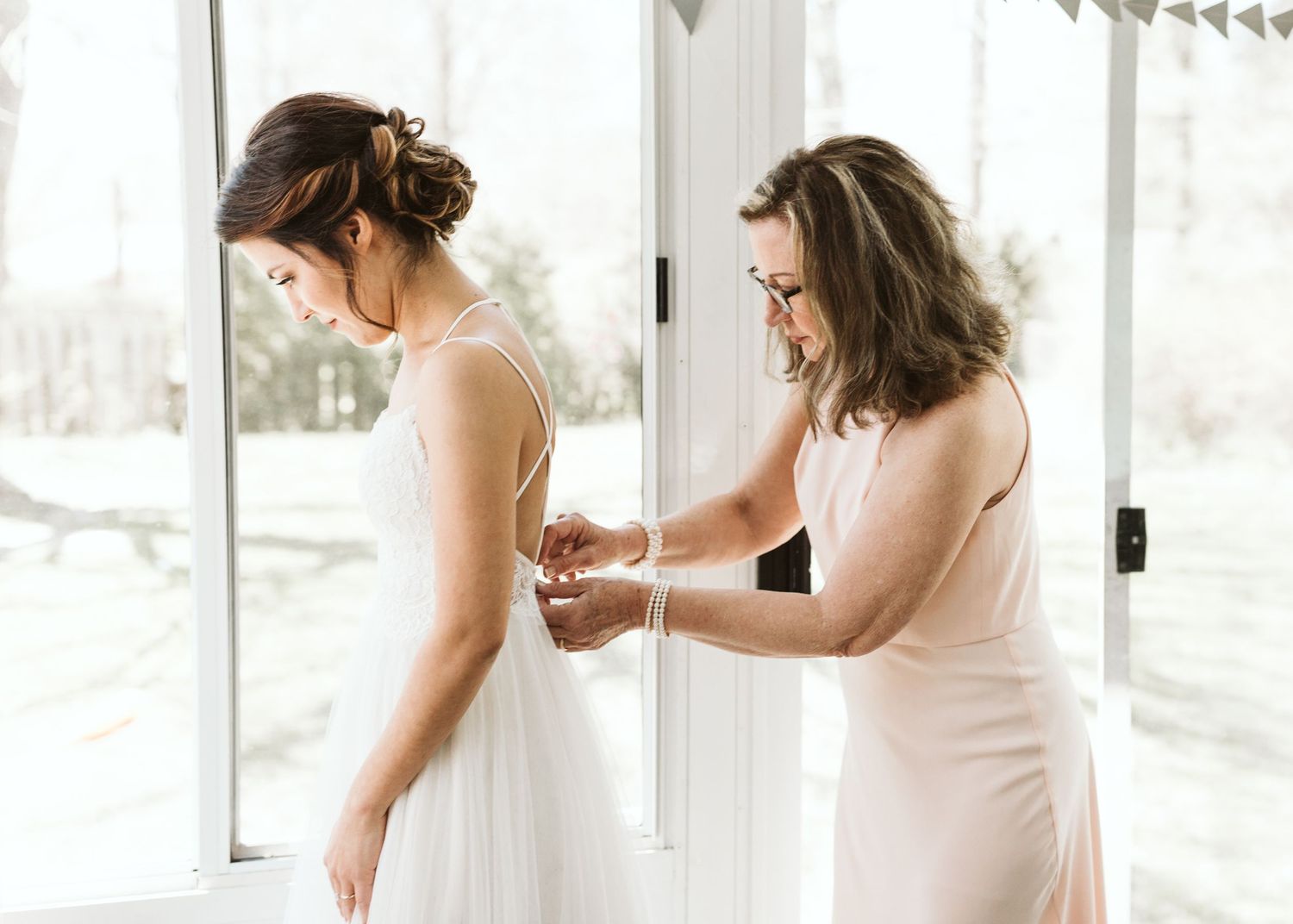 Bride getting ready in bright sunlit room with white decor and flowing dress.