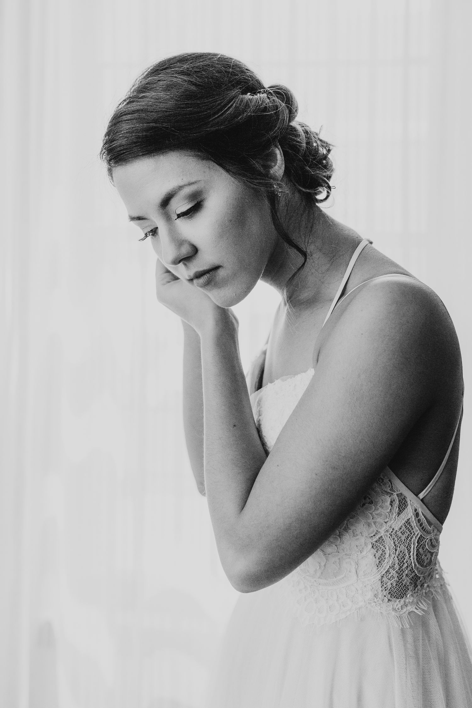 Artistic black and white portrait of a bride in a delicate lace dress looking down with closed eyes.