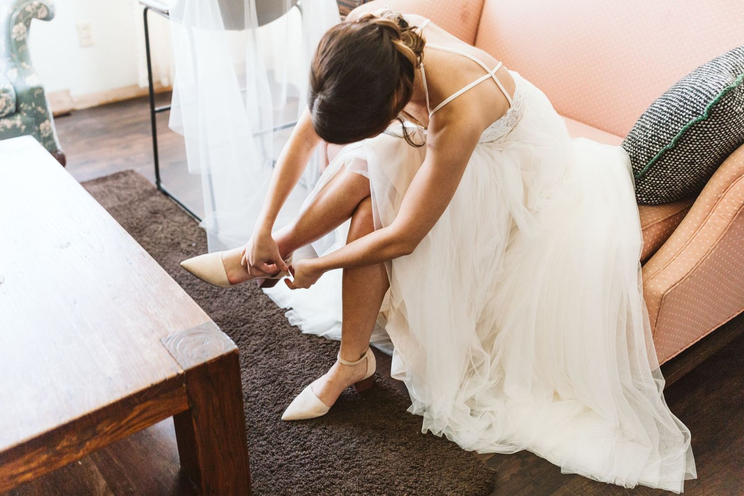 A bride in white dress putting on her shoes while getting ready.