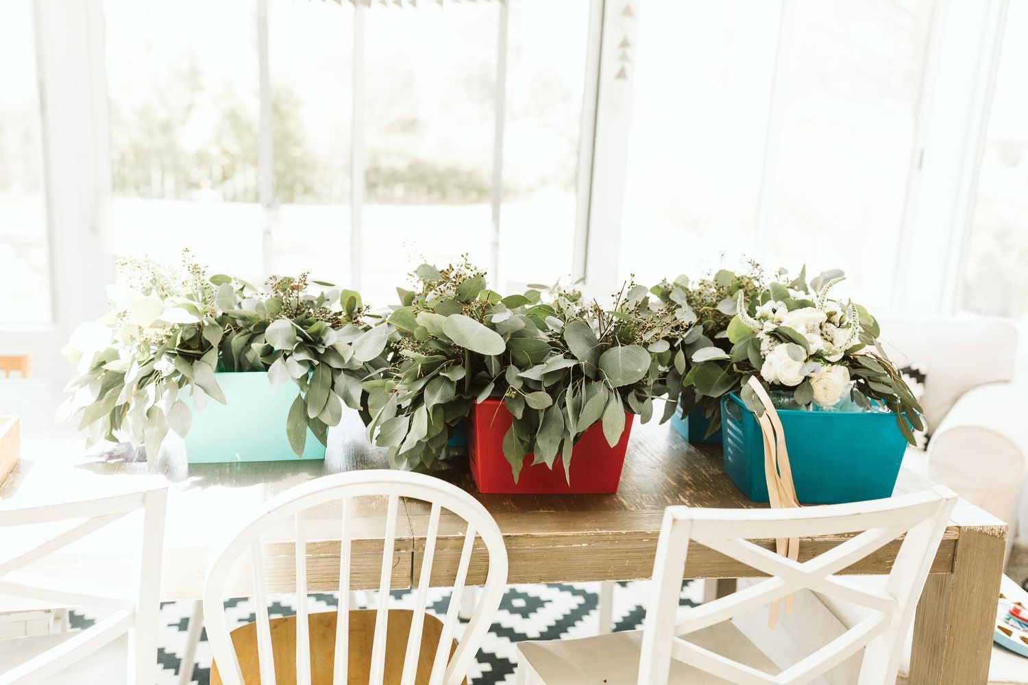 Colorful planters filled with fresh greenery arrangements on white table setting.