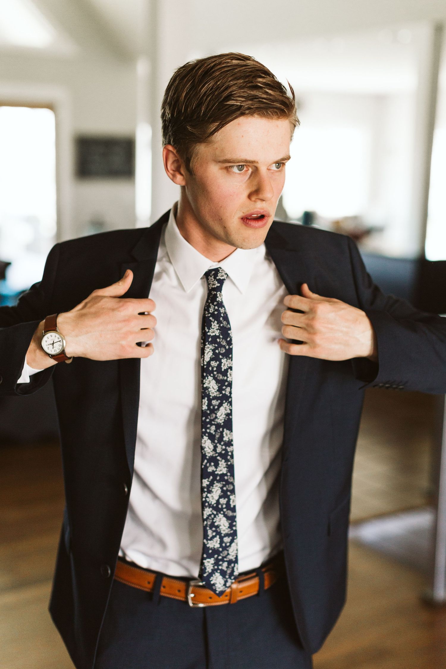 Groom adjusts tie and jacket while wearing navy suit with floral tie.