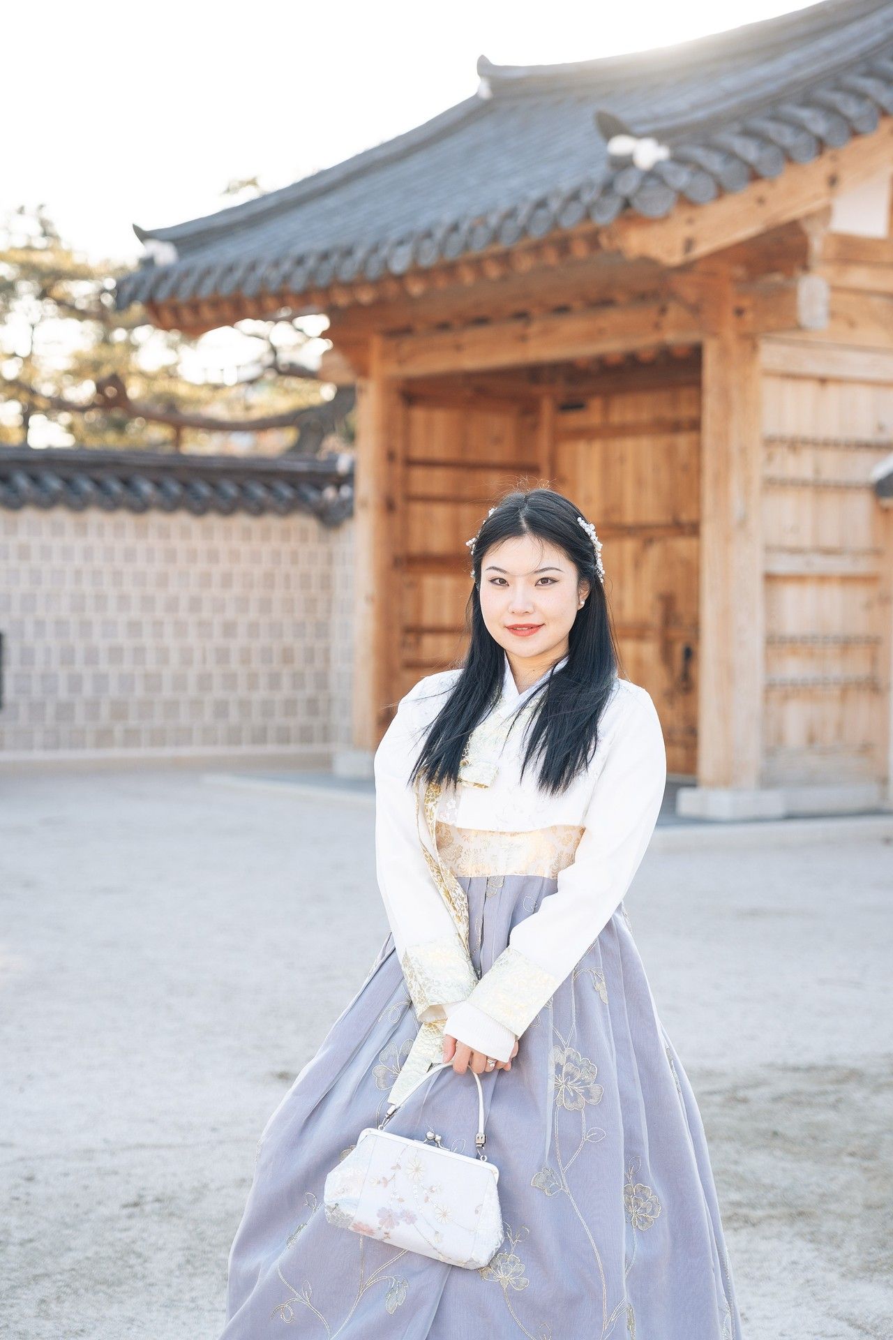 Traditional Korean hanbok dress worn at a historic temple courtyard with grey stone walls and traditional architecture.