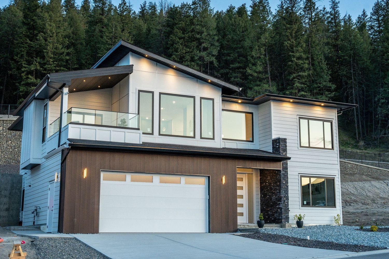 Modern mountain home with angular rooflines and large windows nestled among evergreen trees in a forest setting.