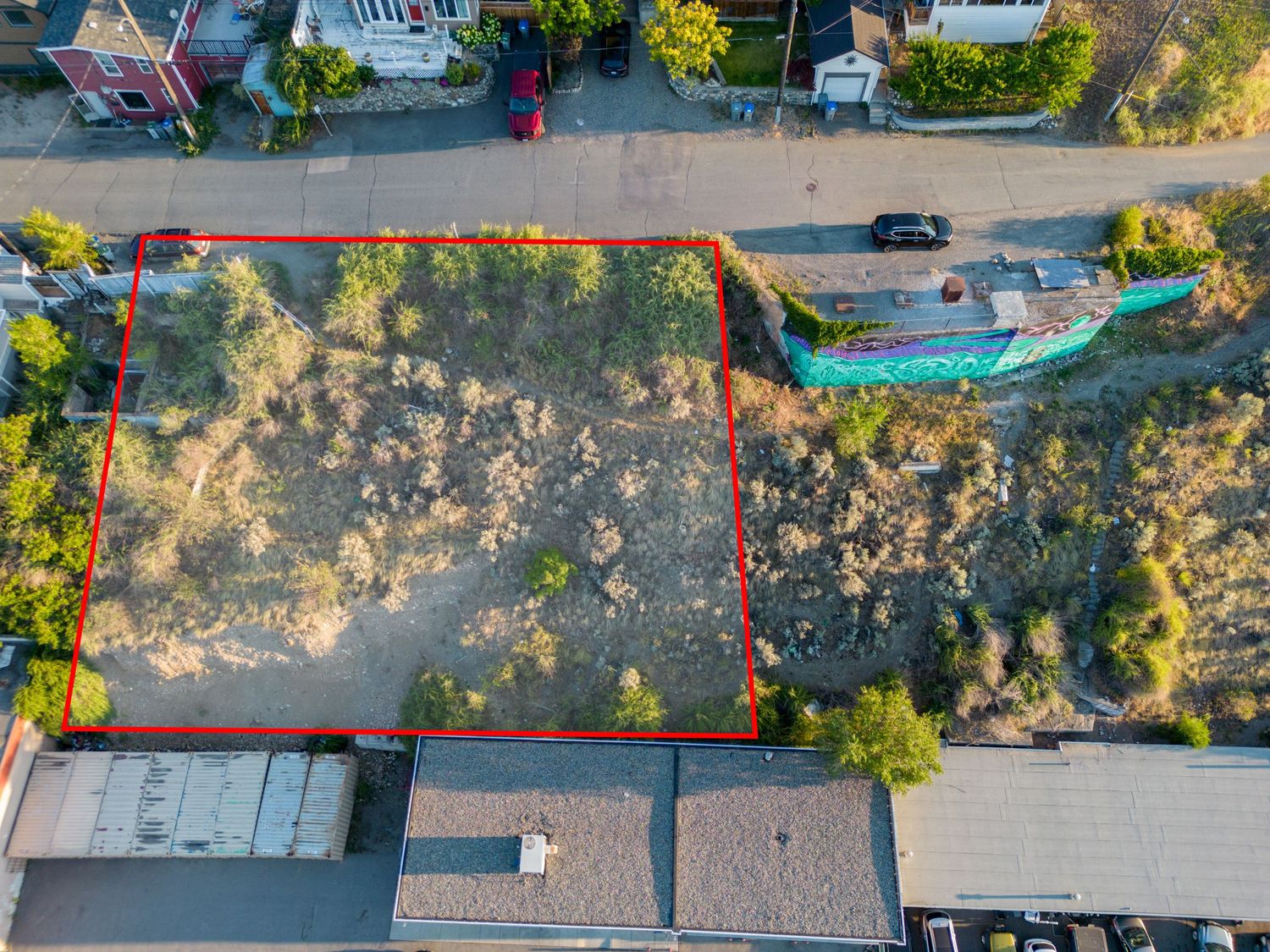 Aerial view of a vacant residential lot with concrete foundation surrounded by trees and neighboring houses.