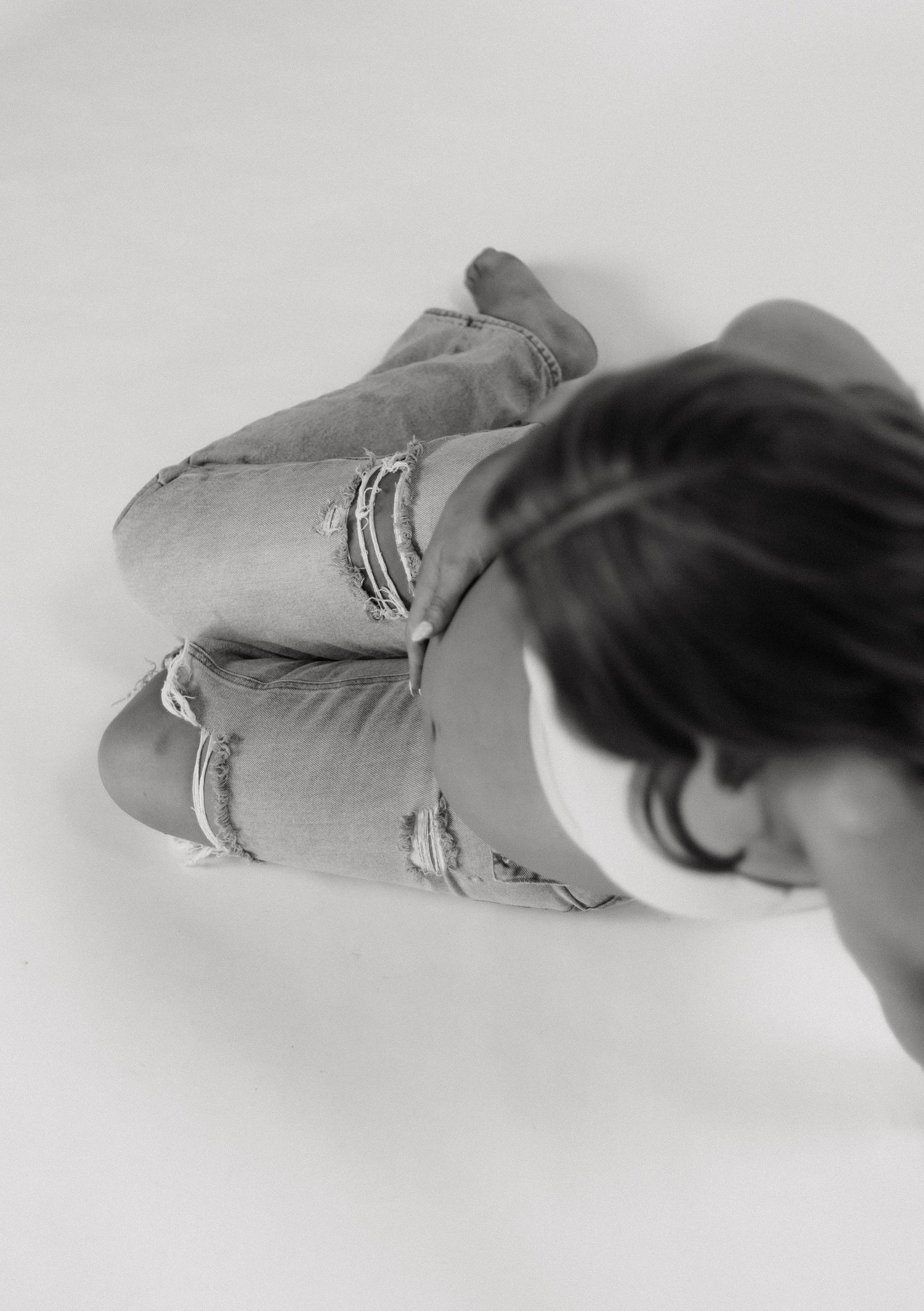 Black and white overhead shot of woman in ripped jeans sitting on floor.