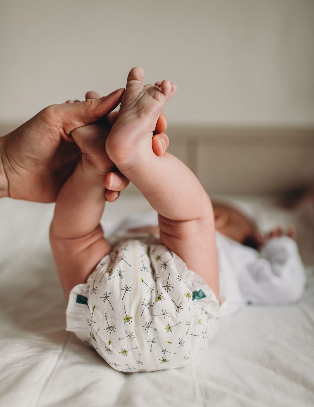 Close-up series of tiny baby feet being held against white bedding with floral pattern details.