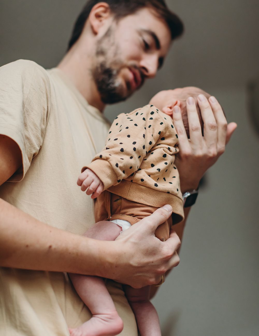 Parent cradles newborn baby wearing polka dot onesie in series of tender moments against neutral background.