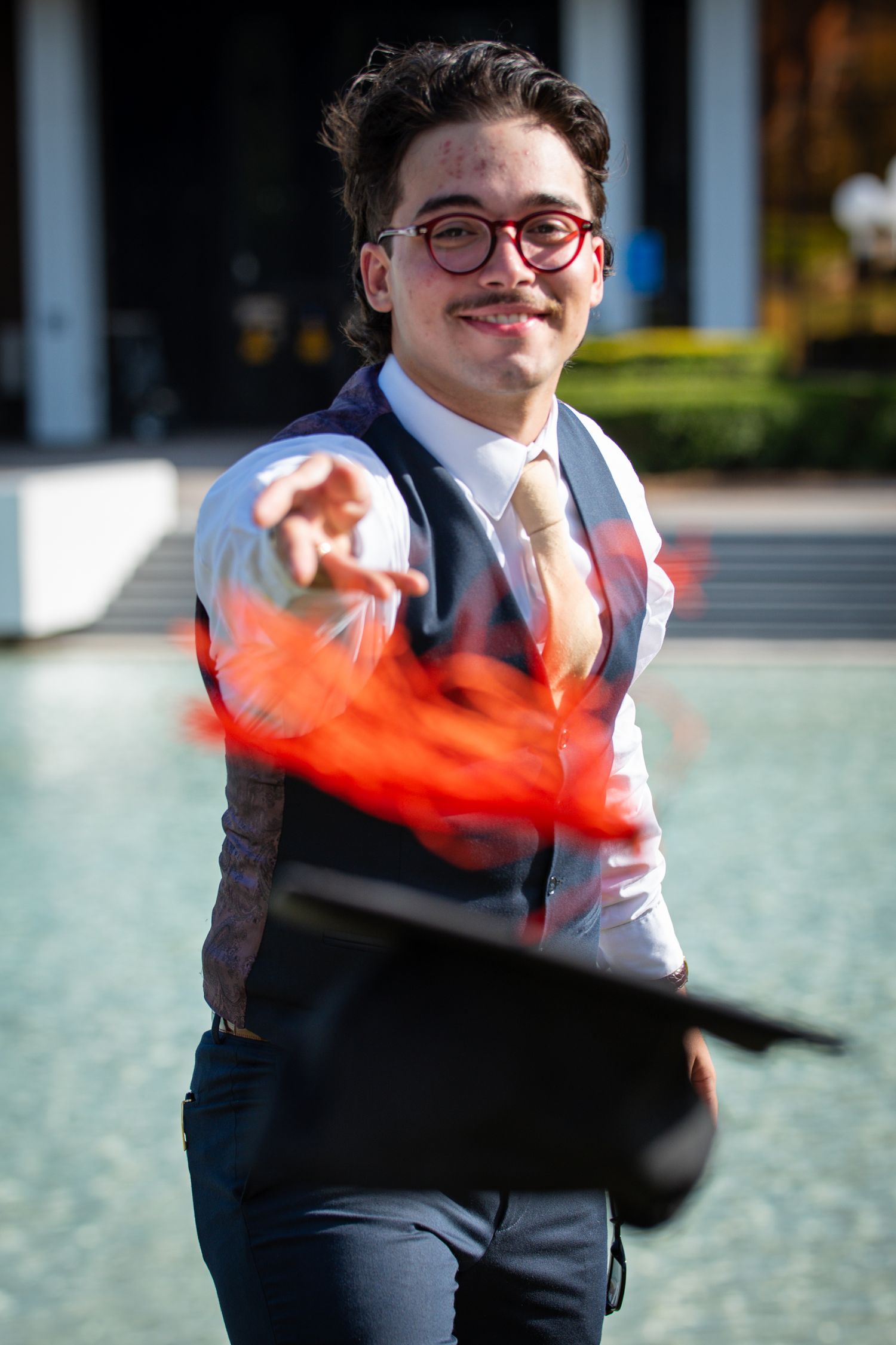 A person in business attire with glasses stands outdoors with a motion-blurred red object in the foreground.