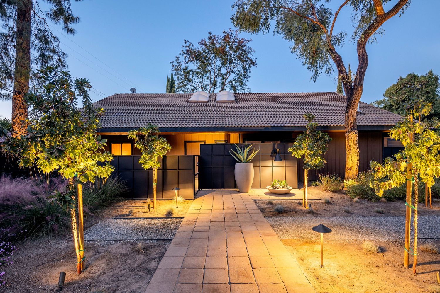 Modern desert home illuminated at dusk with warm landscape lighting highlighting native plants and walkway.