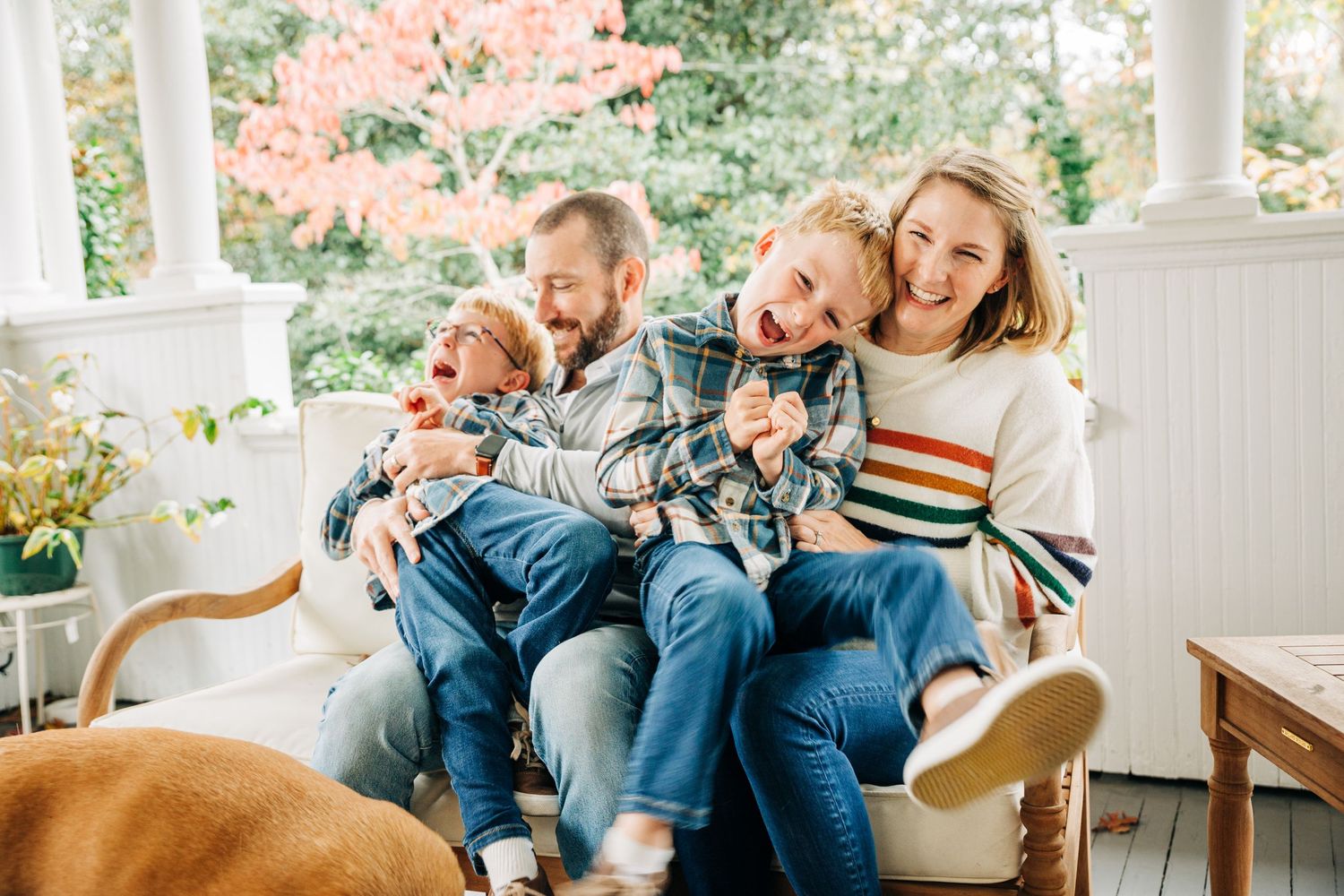 A joyful family sits together on a cozy porch swing wearing casual denim and sweaters on an autumn day.