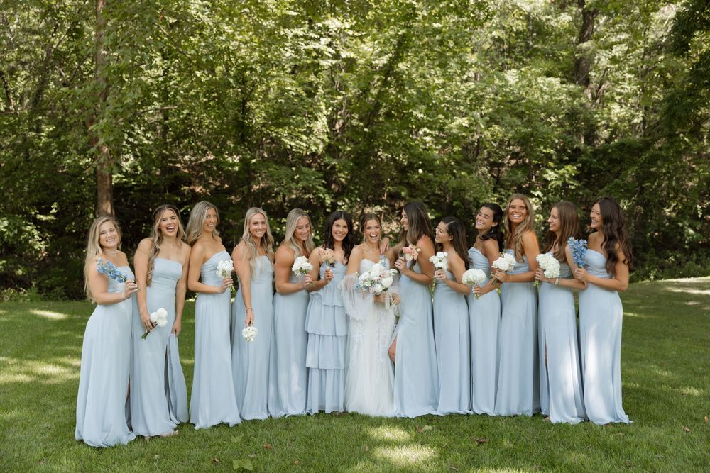 A row of bridesmaids in light blue dresses pose together for outdoor oklahoma wedding photos in a garden setting.