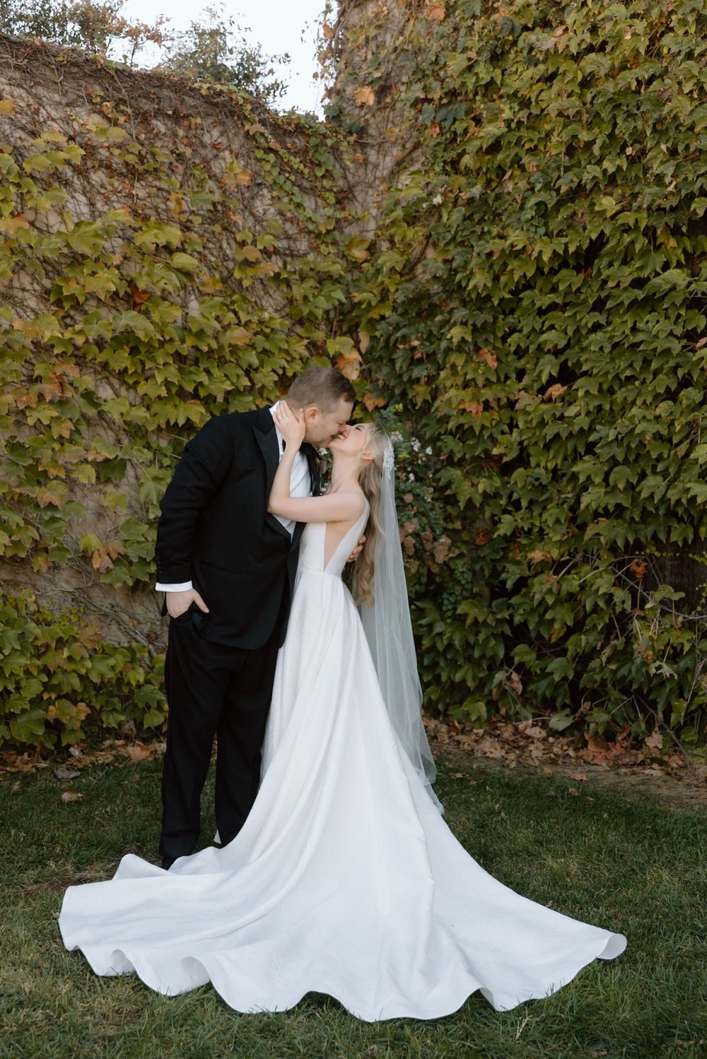 Elegant couple shares romantic moments in garden setting with lush green ivy wall backdrop during autumn wedding ceremony.