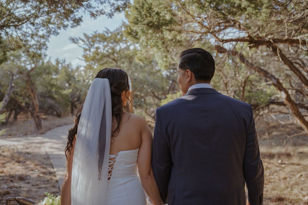 Newlywed couple walks hand in hand through a sunlit forest path during golden hour wedding photography session.