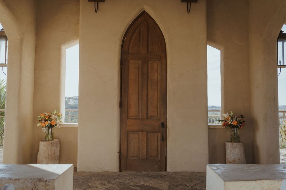 A bright white hallway with wooden doors, arched windows, and stone columns in a Mediterranean architectural style.