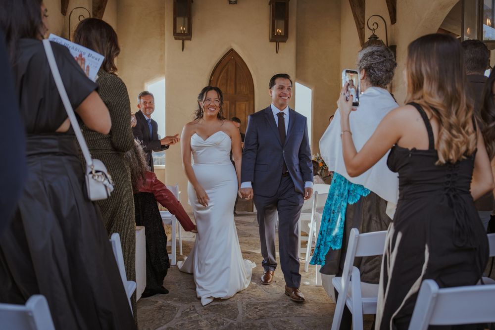 Wedding party members in formal attire gather and socialize during an elegant indoor reception.