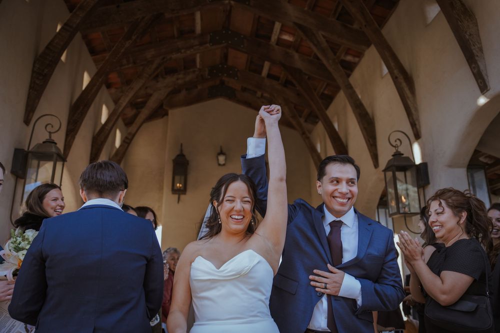 Wedding guests celebrate and dance together during a joyful reception in an elegant vaulted venue.