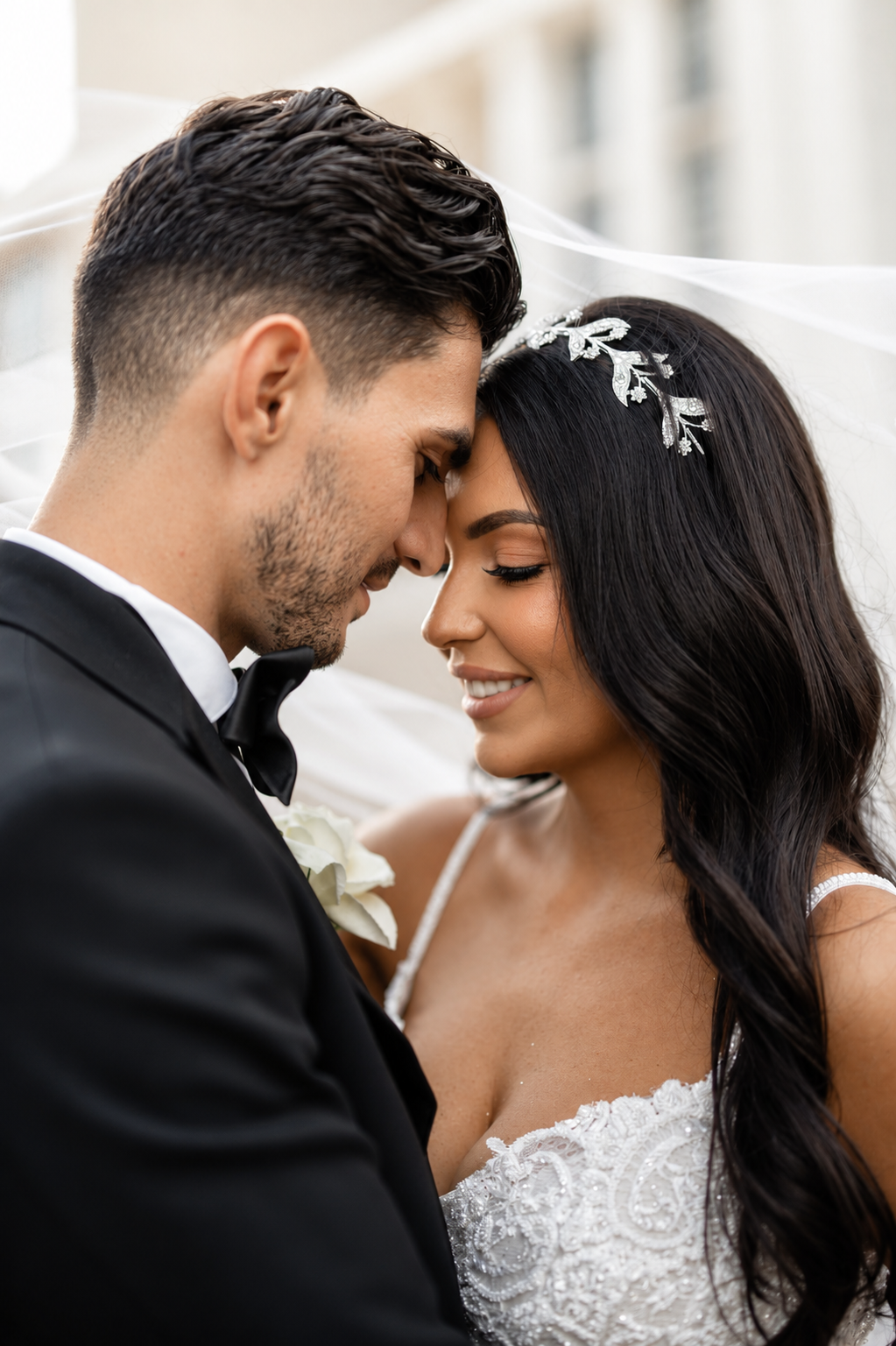 Bride and groom touching foreheads tenderly under a white veil on their wedding day.