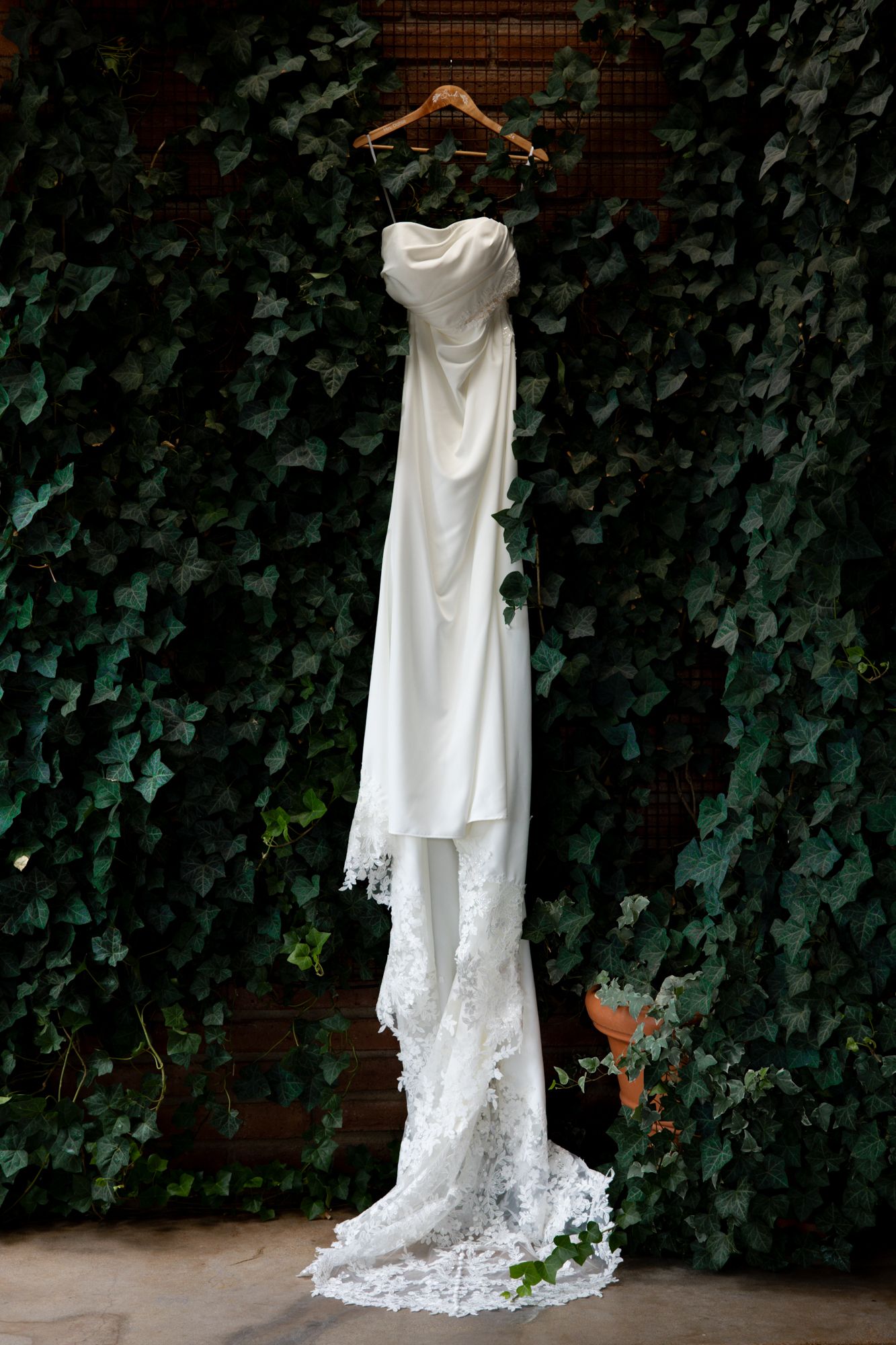 White lace wedding dress with sweetheart neckline and train displayed against ivy-covered brick wall.