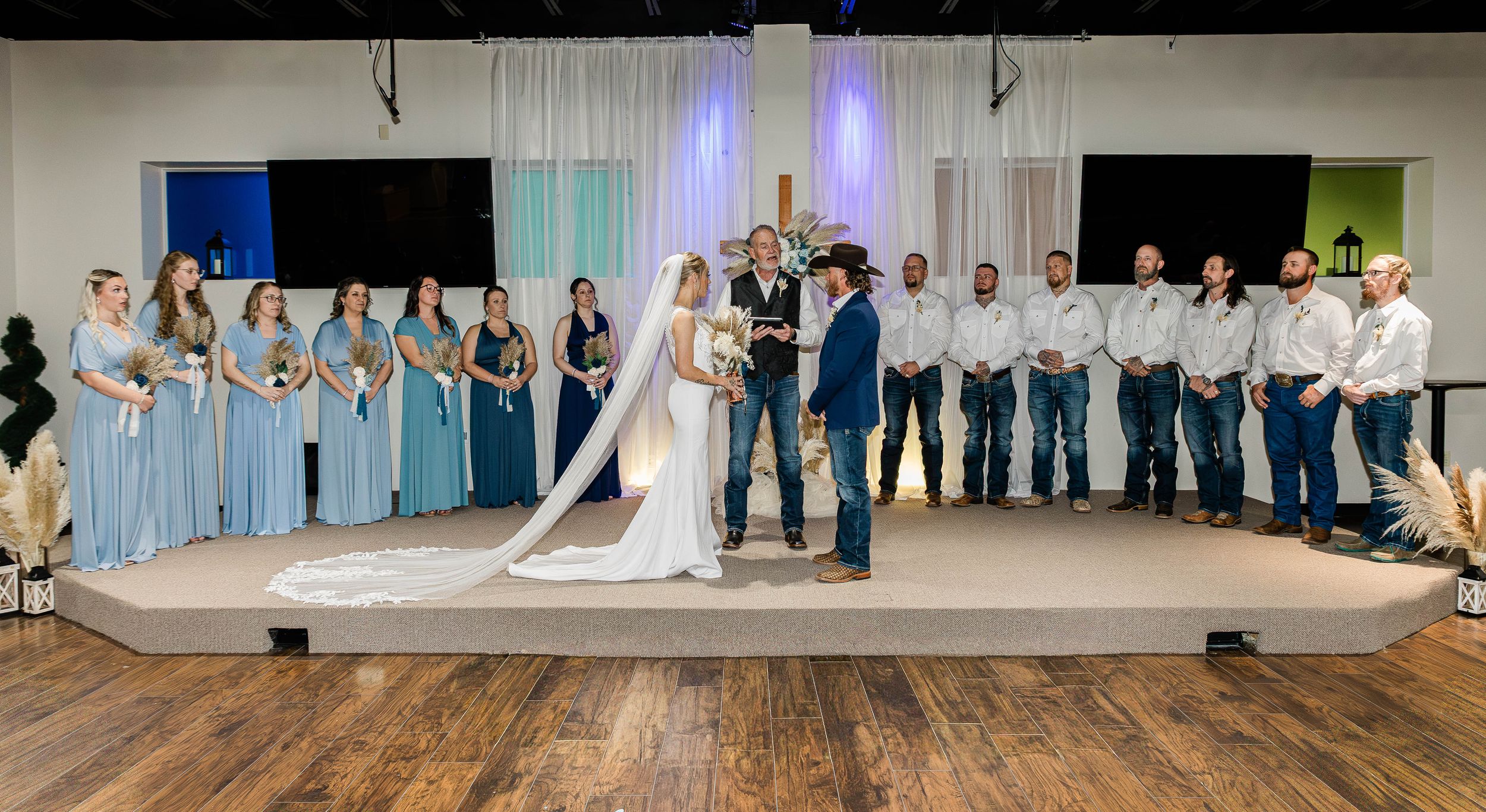 Wide shot of wedding ceremony with bridal party in blue dresses and groomsmen in white shirts.