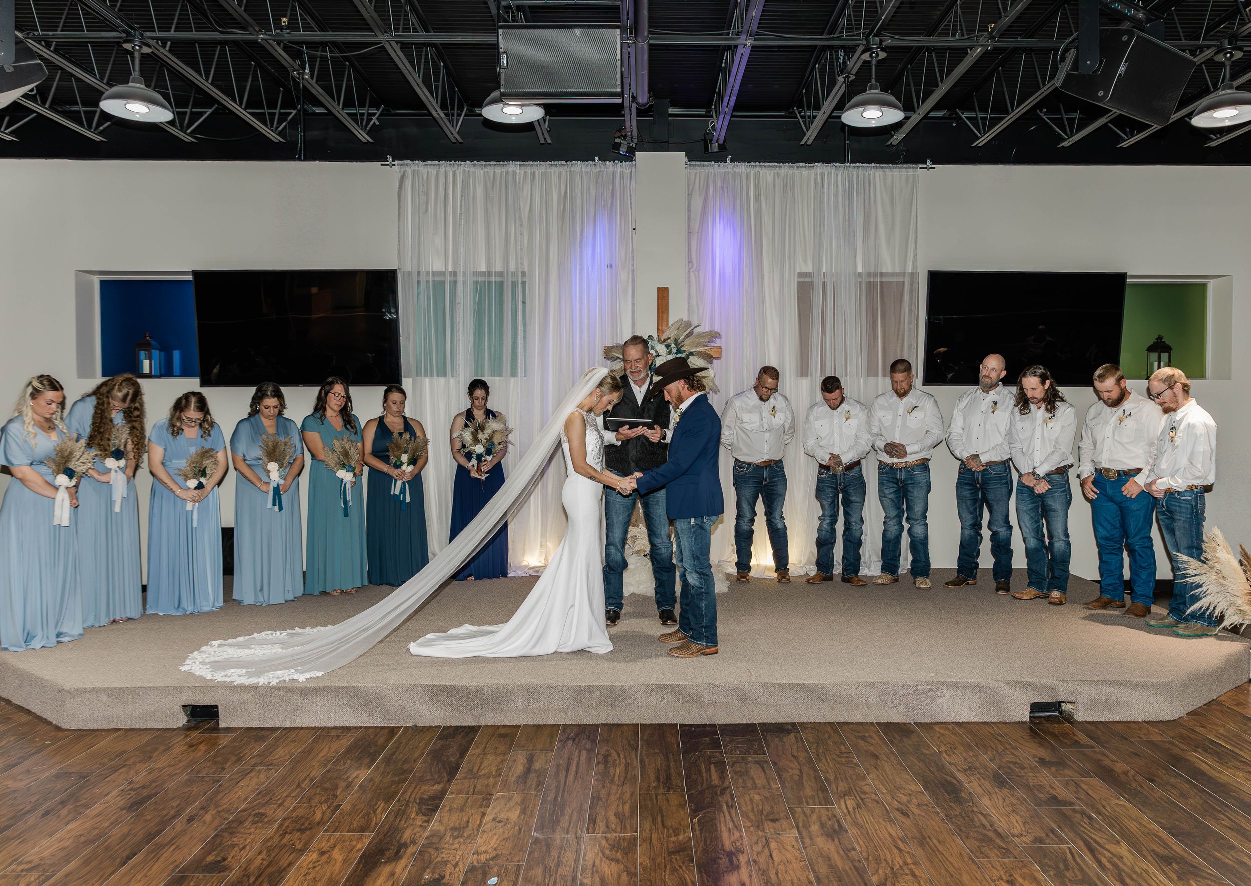 Full wedding party photo with bride and groom centered on stage with attendants in blue attire.
