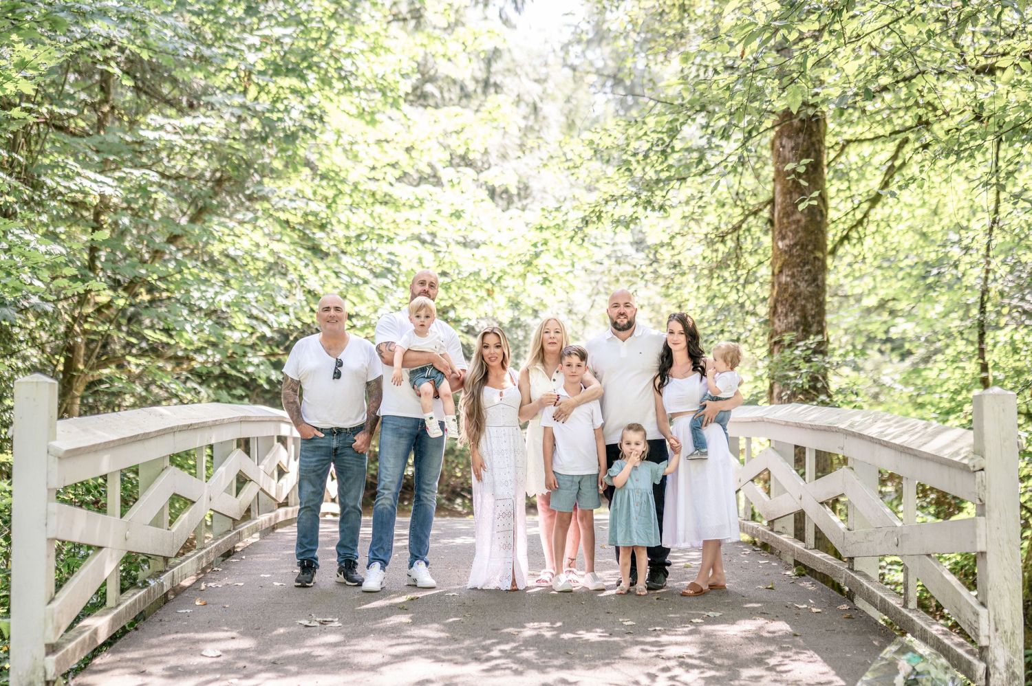 A group in coordinated white and blue outfits poses together on a wooden bridge in a lush forest setting.