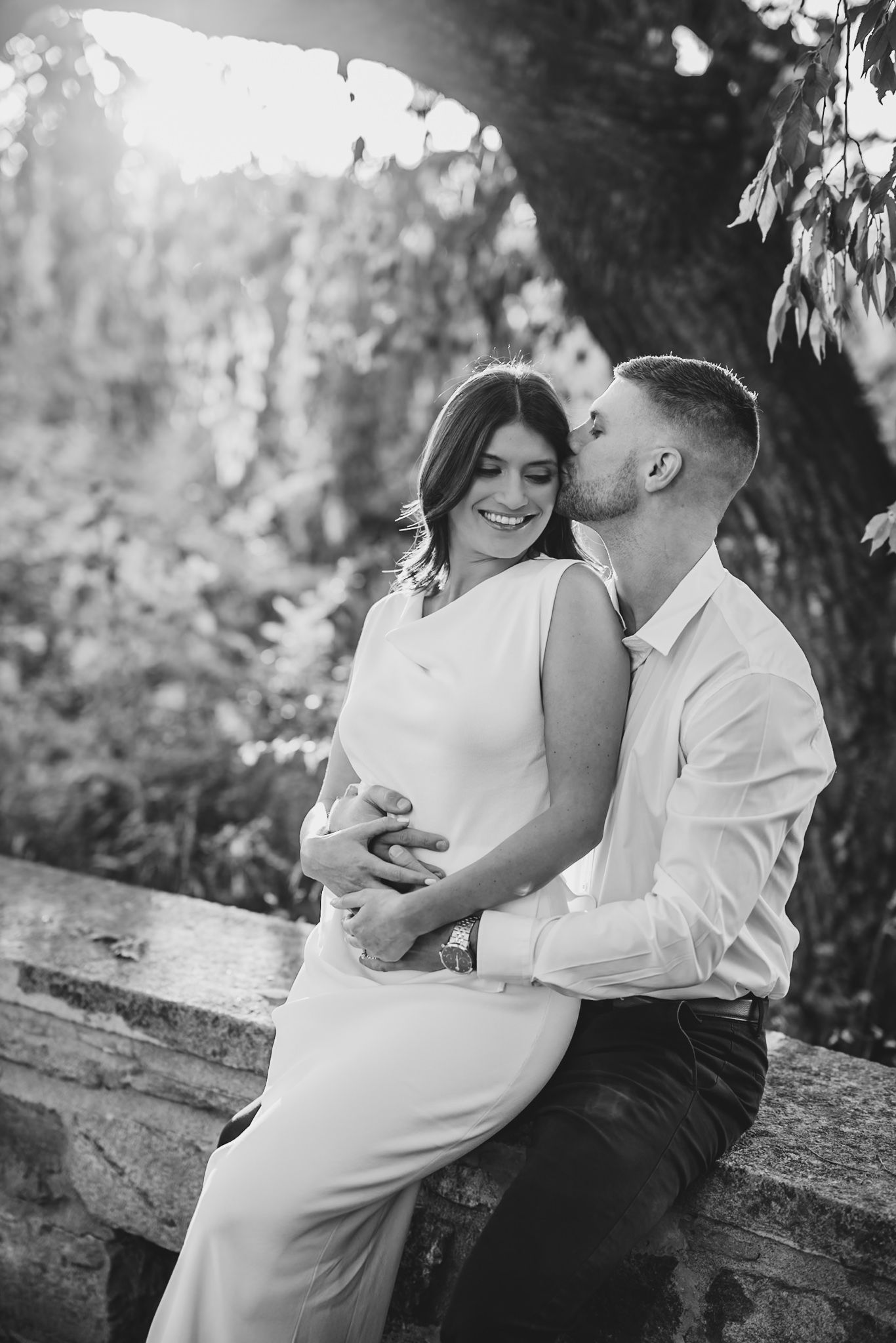 Black and white intimate portraits captured on rustic stone wall under trees.