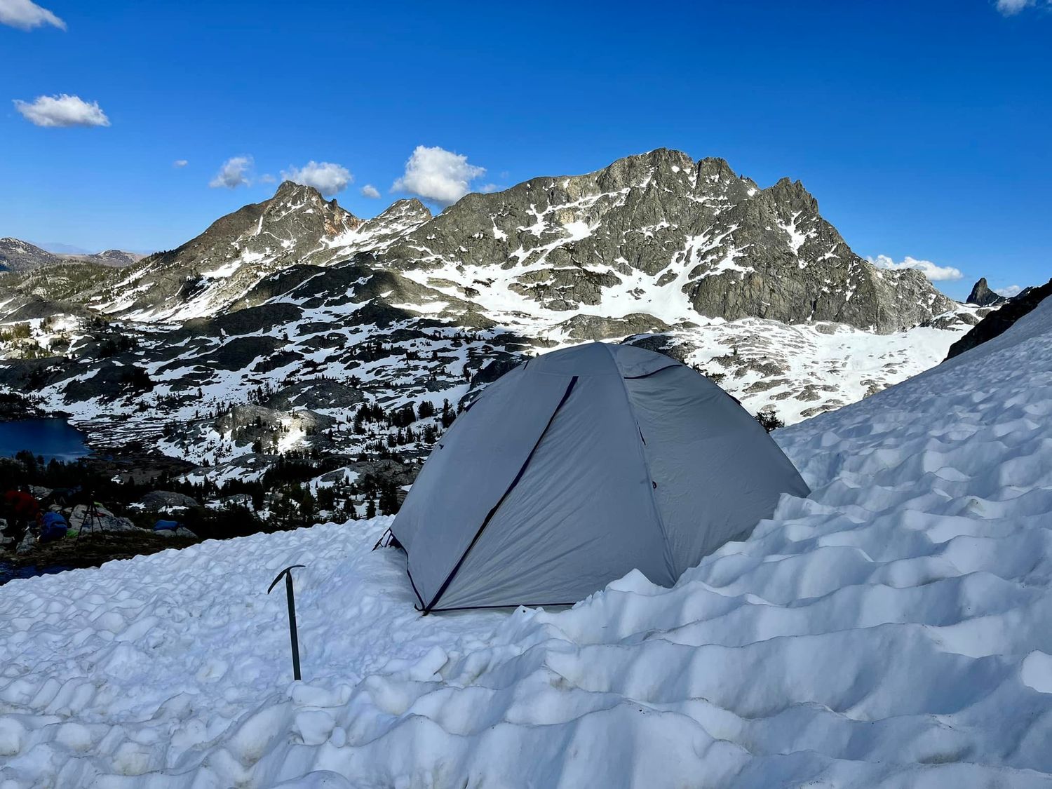 A tent set up in snowy alpine mountains during a winter backcountry camping adventure under clear skies.